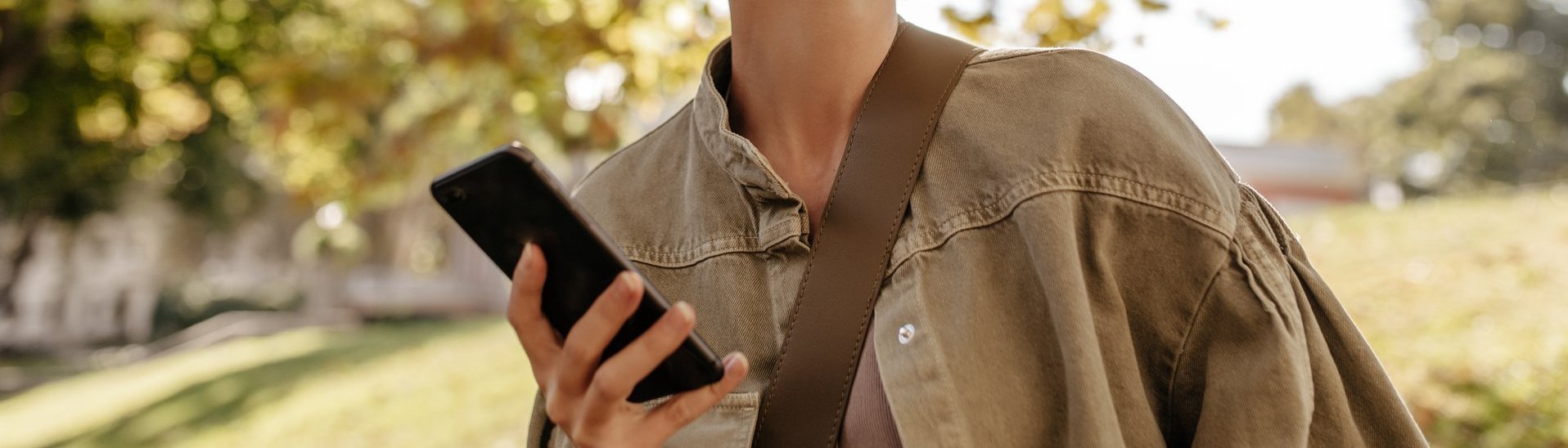 optimistische-frau-mit-bruenetten-haaren-in-denim-oliven-kleidern-laechelt-und-haelt-telefon-draussen-frau-in-leichten-kopfhoerern-posiert-im-freien